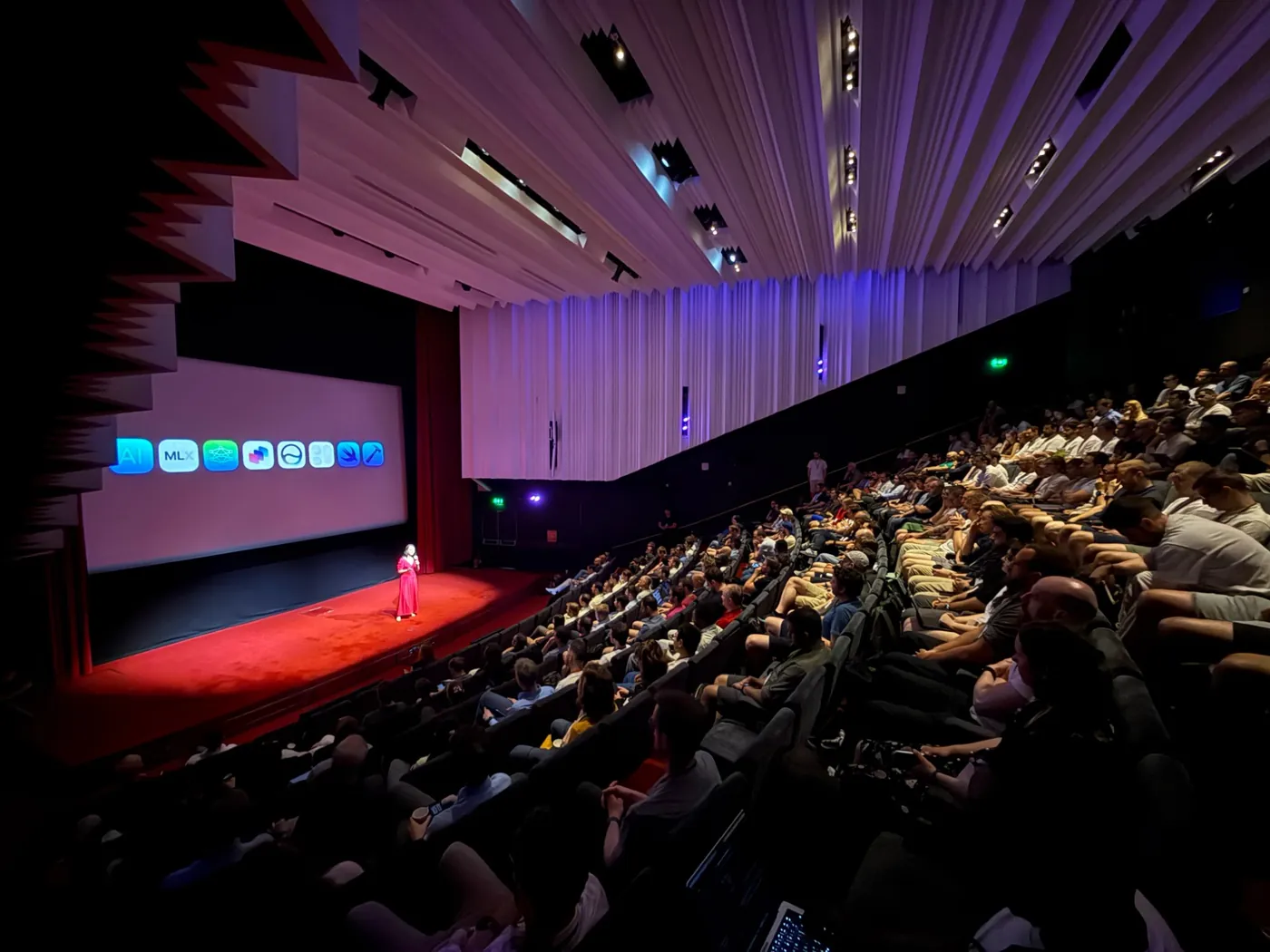 A packed auditorium at a “Meet with Apple” event: a speaker on stage in front of the screen