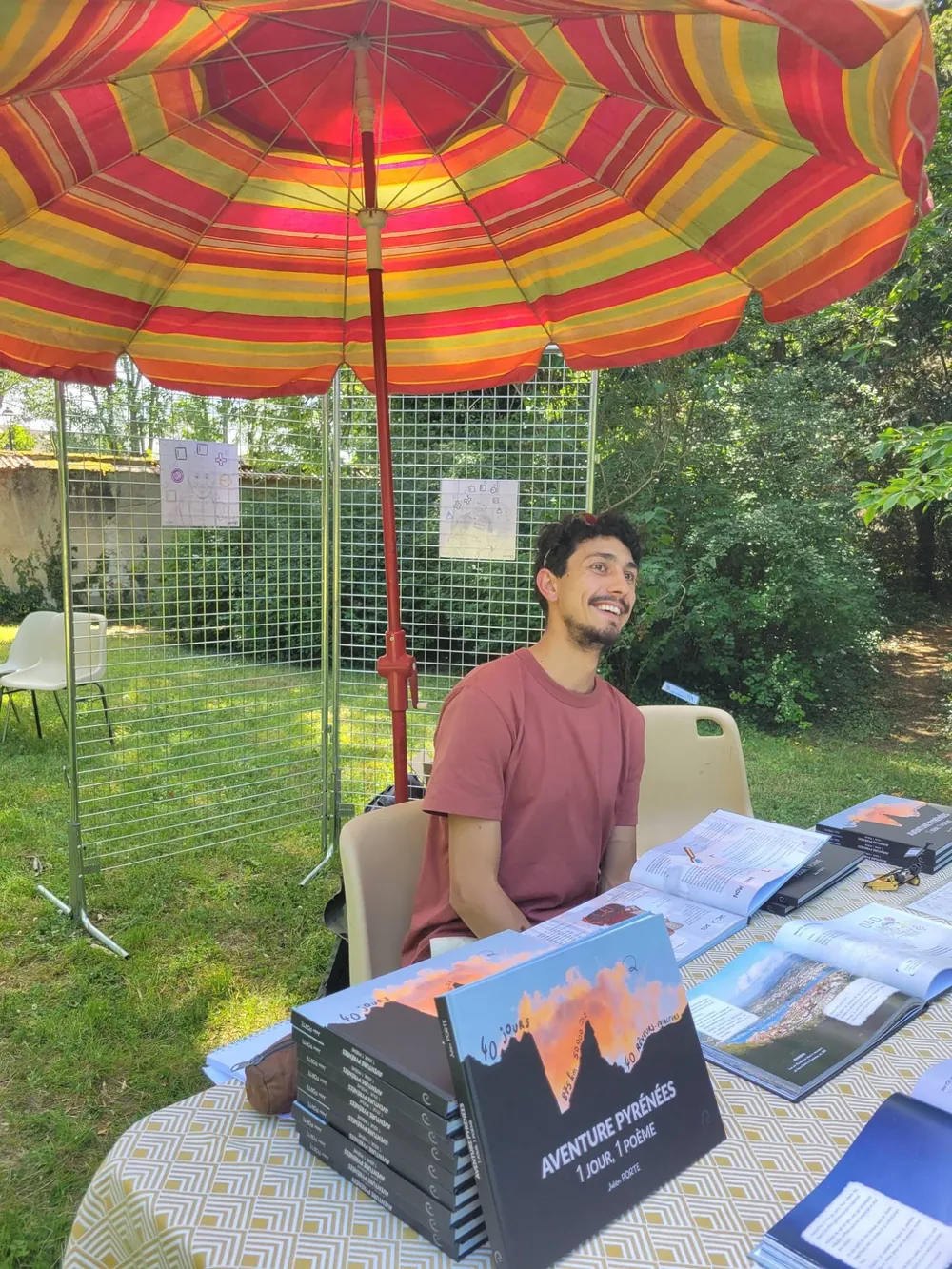 Julien Porte smiling behind his table of books, under the stand’s parasol