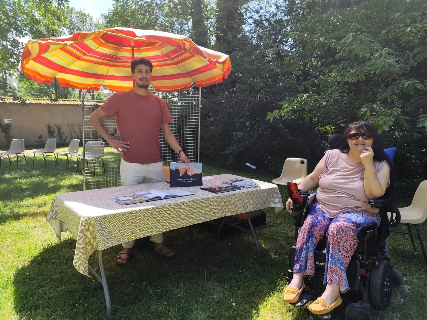 Julien Porte and Magali at the Rêveurs-Voyageurs stand in the garden, under a parasol