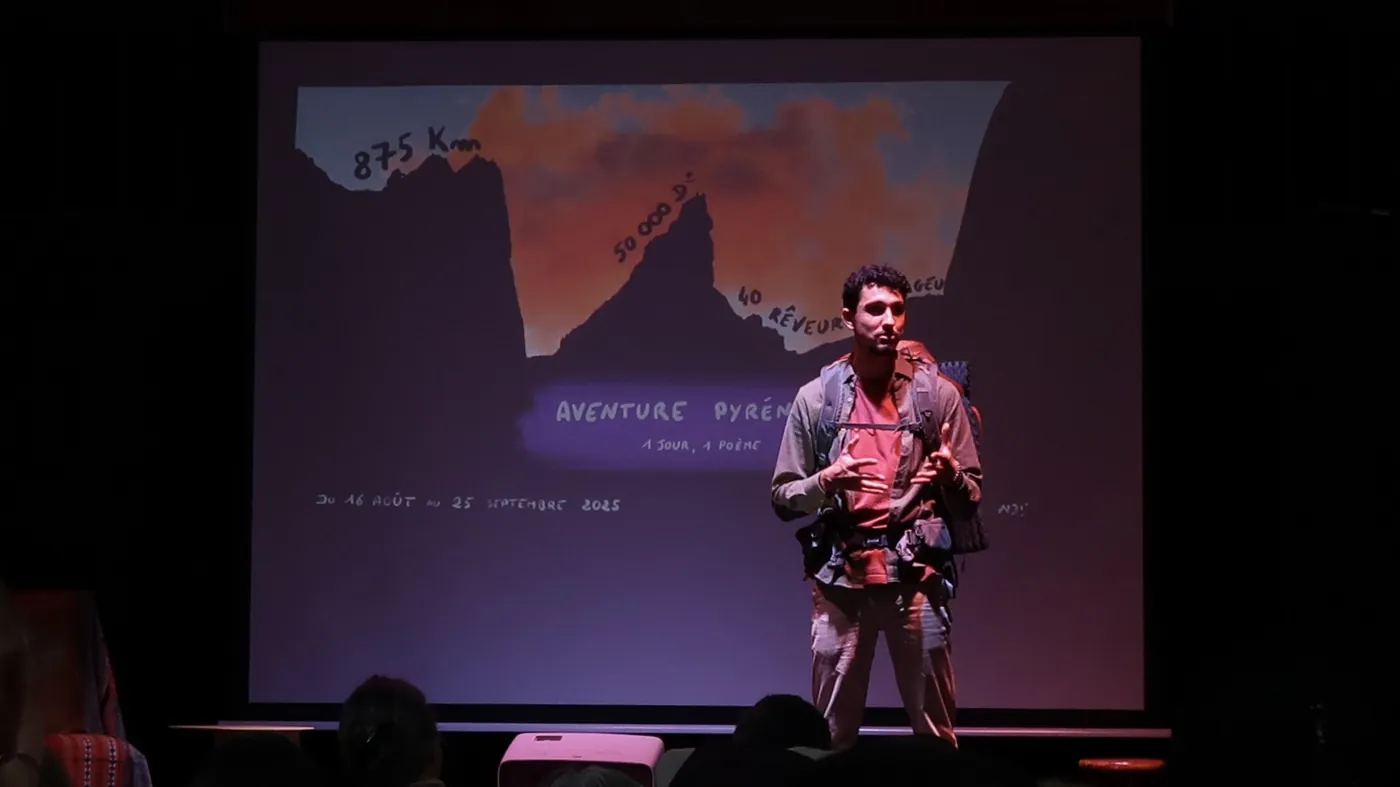 Julien Porte on stage in hiking gear in front of the Pyrenees Adventure projection